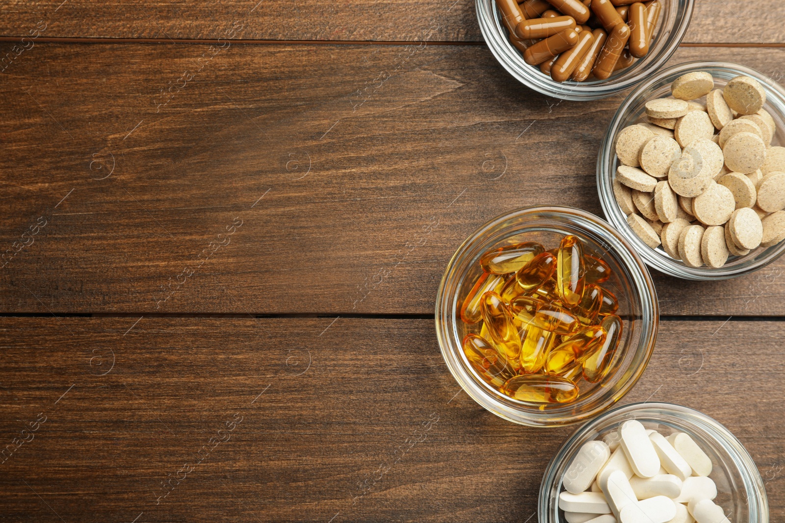 Photo of Different dietary supplements in glass bowls on wooden table, flat lay. Space for text