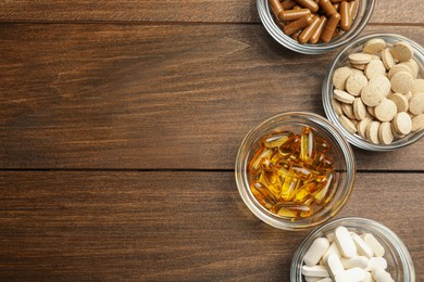 Photo of Different dietary supplements in glass bowls on wooden table, flat lay. Space for text