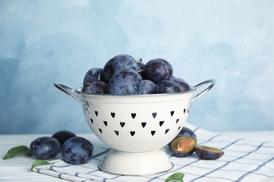 Delicious ripe plums in colander on table against light background