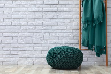 Stylish knitted pouf and ladder with plaid near white brick wall indoors, space for text. Interior design