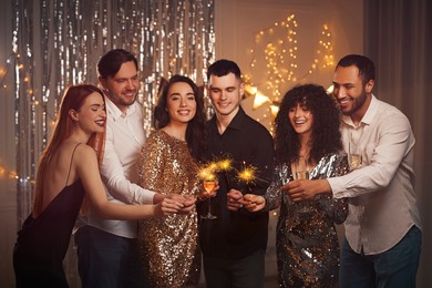 Photo of Happy friends with glasses of wine and sparklers celebrating birthday indoors