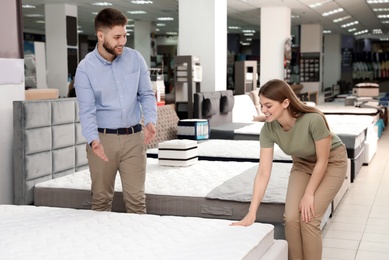 Young salesman helping customer to choose new modern orthopedic mattress in store