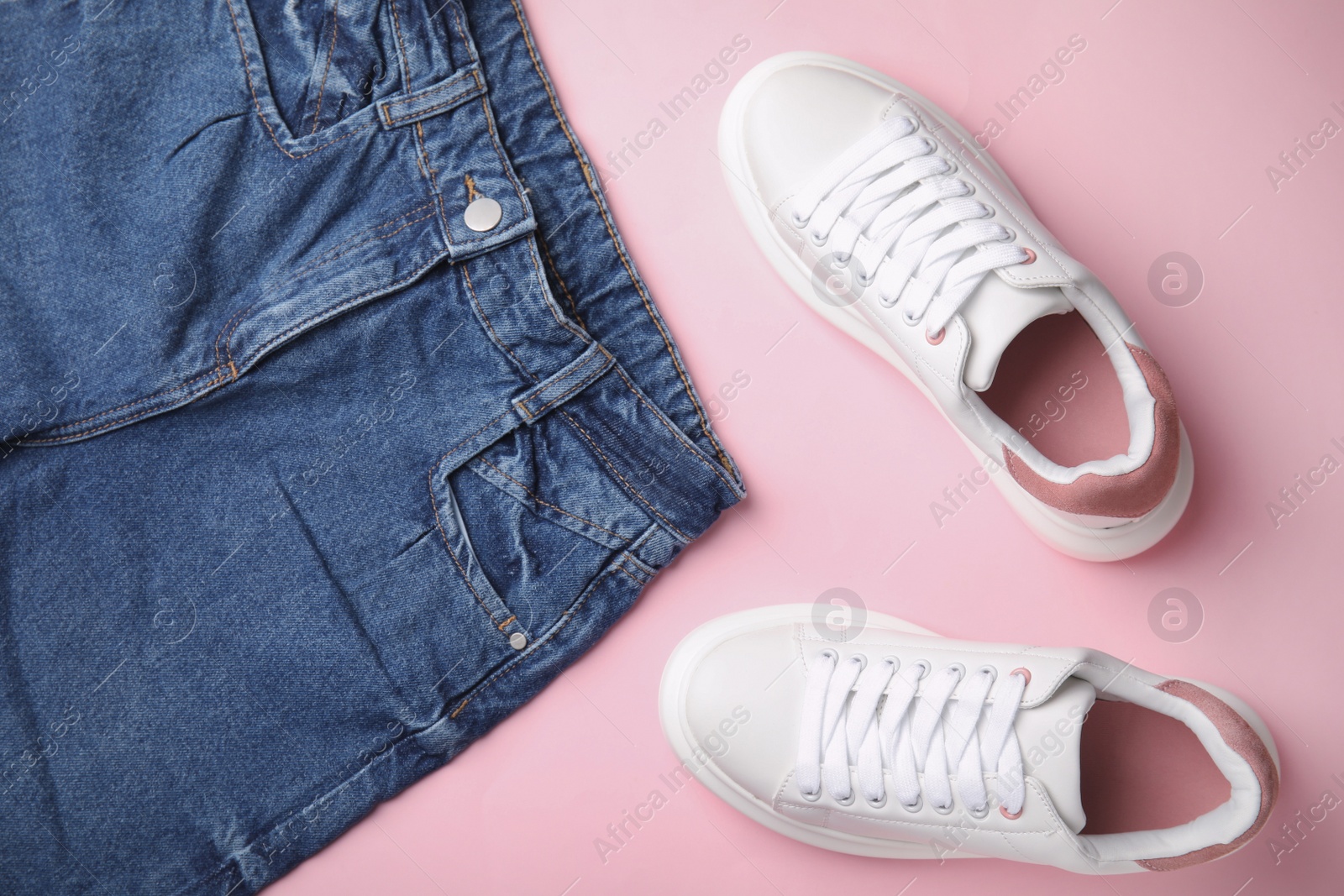 Photo of Stylish white sneakers and jeans on pink background, flat lay