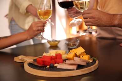 Different delicious cheeses on table and blurred friends toasting with wine on background