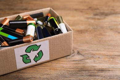 Image of Used batteries in cardboard box with recycling symbol on wooden table, closeup. Space for text