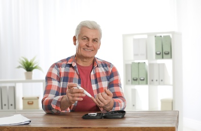 Photo of Senior man using lancet pen at table. Diabetes control