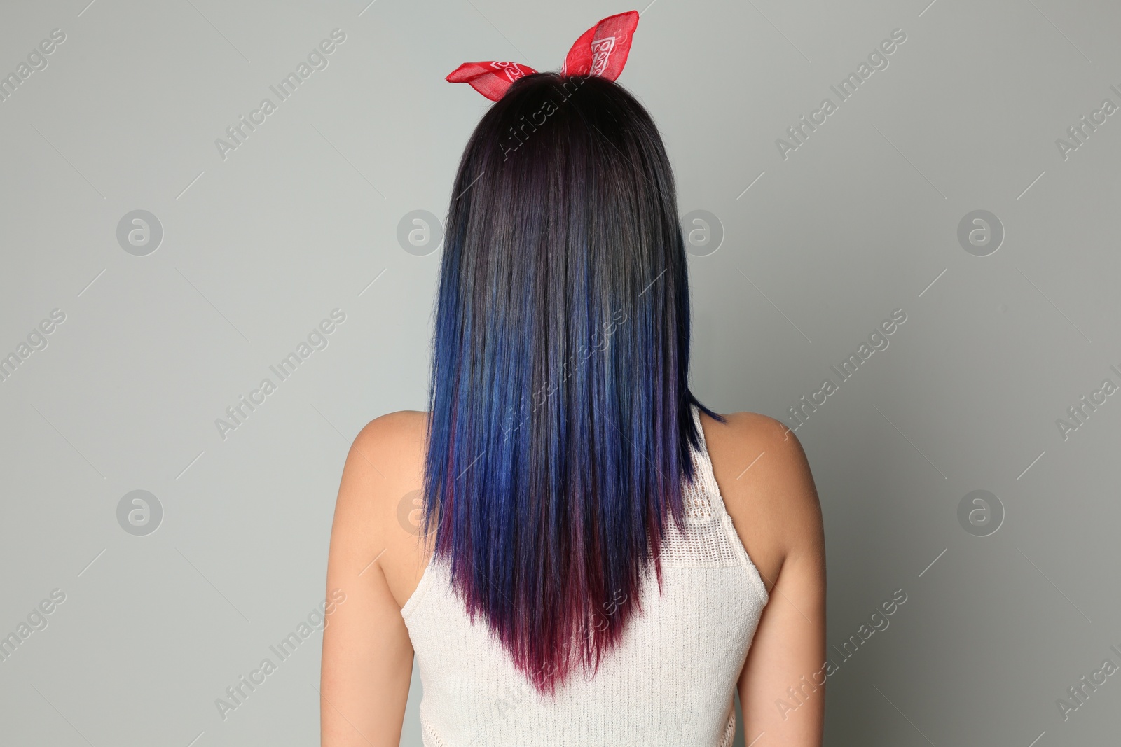 Photo of Young woman with bright dyed hair on grey background, back view