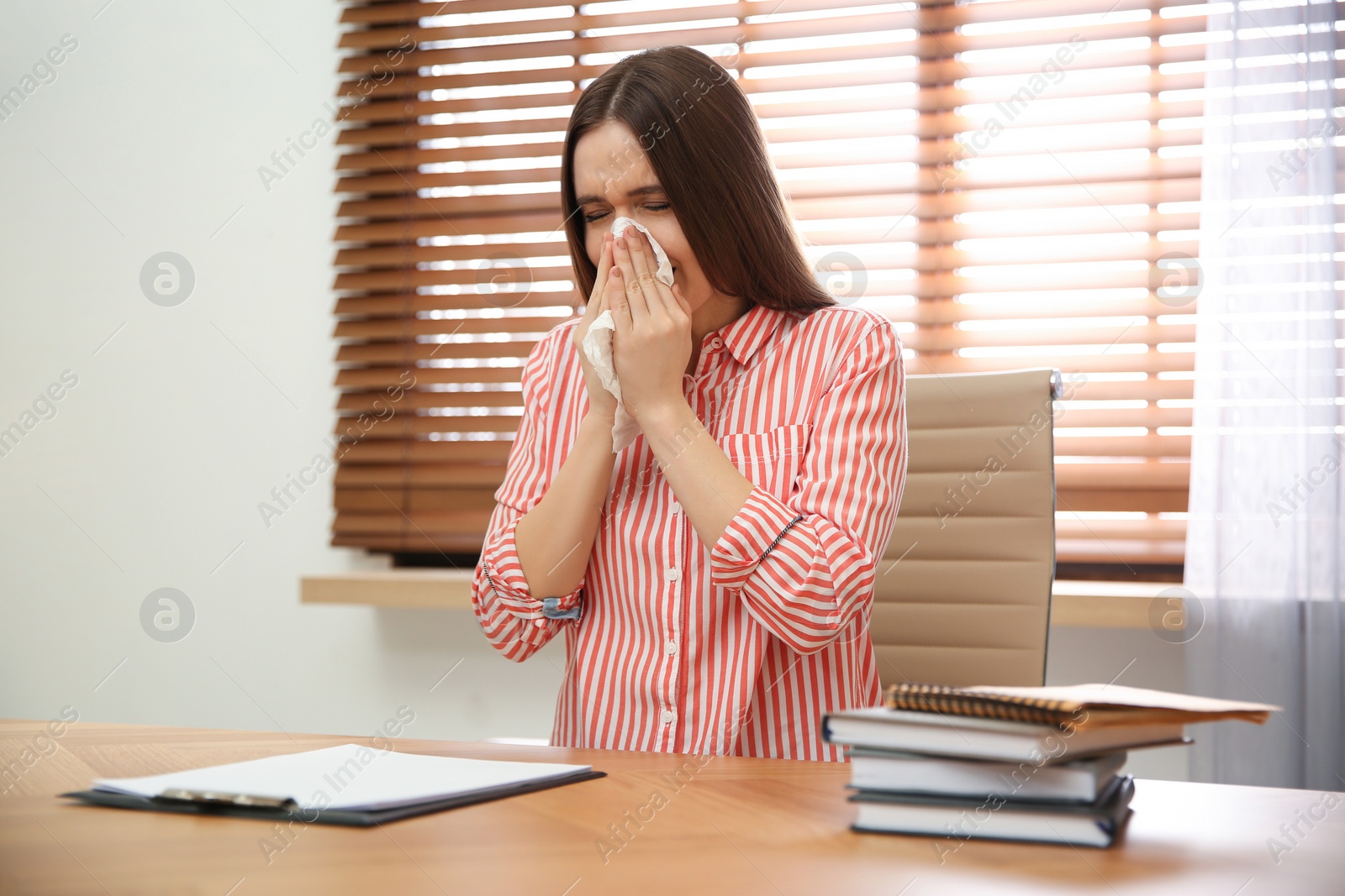 Photo of Sick young woman sneezing at workplace. Influenza virus