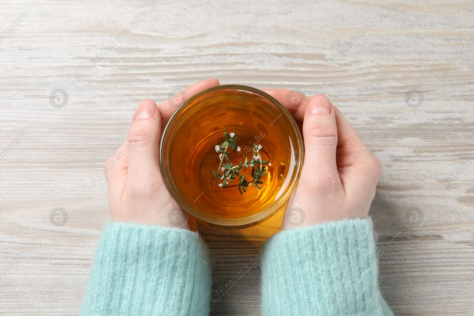 Photo of Woman holding cup of tasty herbal tea with thyme at white wooden table, closeup