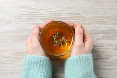 Photo of Woman holding cup of tasty herbal tea with thyme at white wooden table, closeup