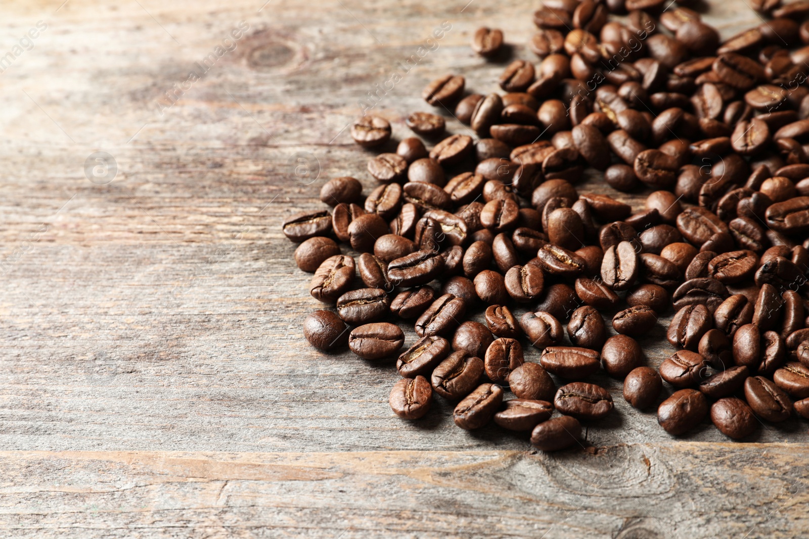Photo of Pile of roasted coffee beans on wooden background, space for text