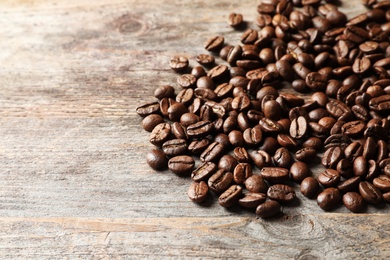 Pile of roasted coffee beans on wooden background, space for text