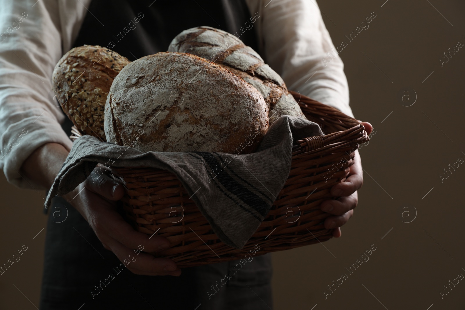 Photo of Man holding wicker basket with different types of bread on brown background, closeup