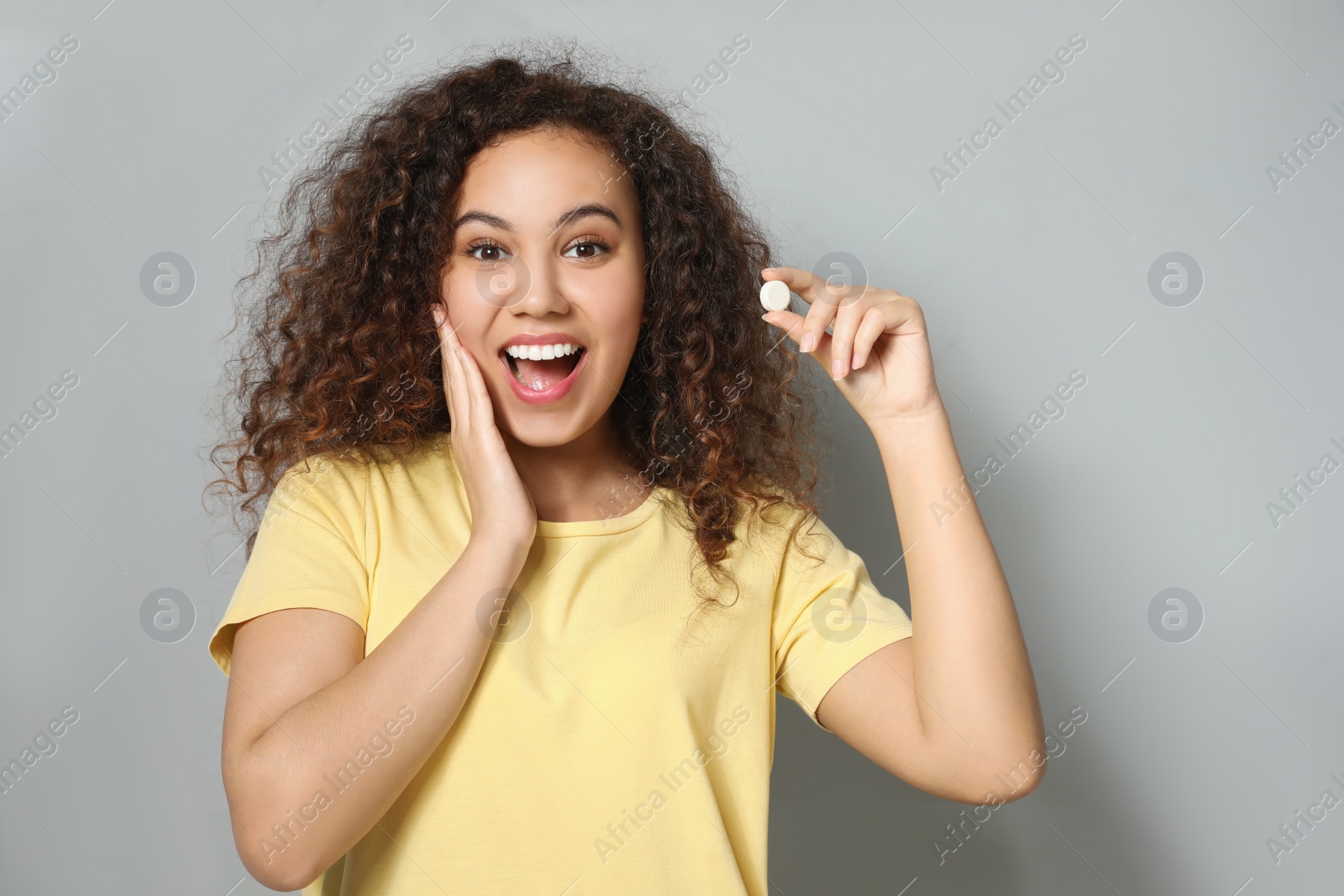 Photo of Emotional African-American woman with vitamin pill on light grey background