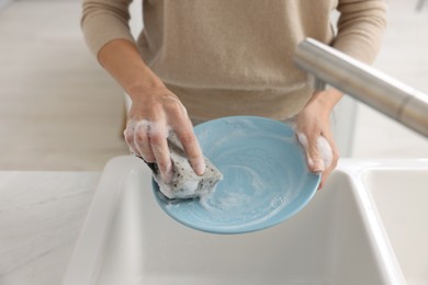 Woman washing plate above sink in modern kitchen, closeup