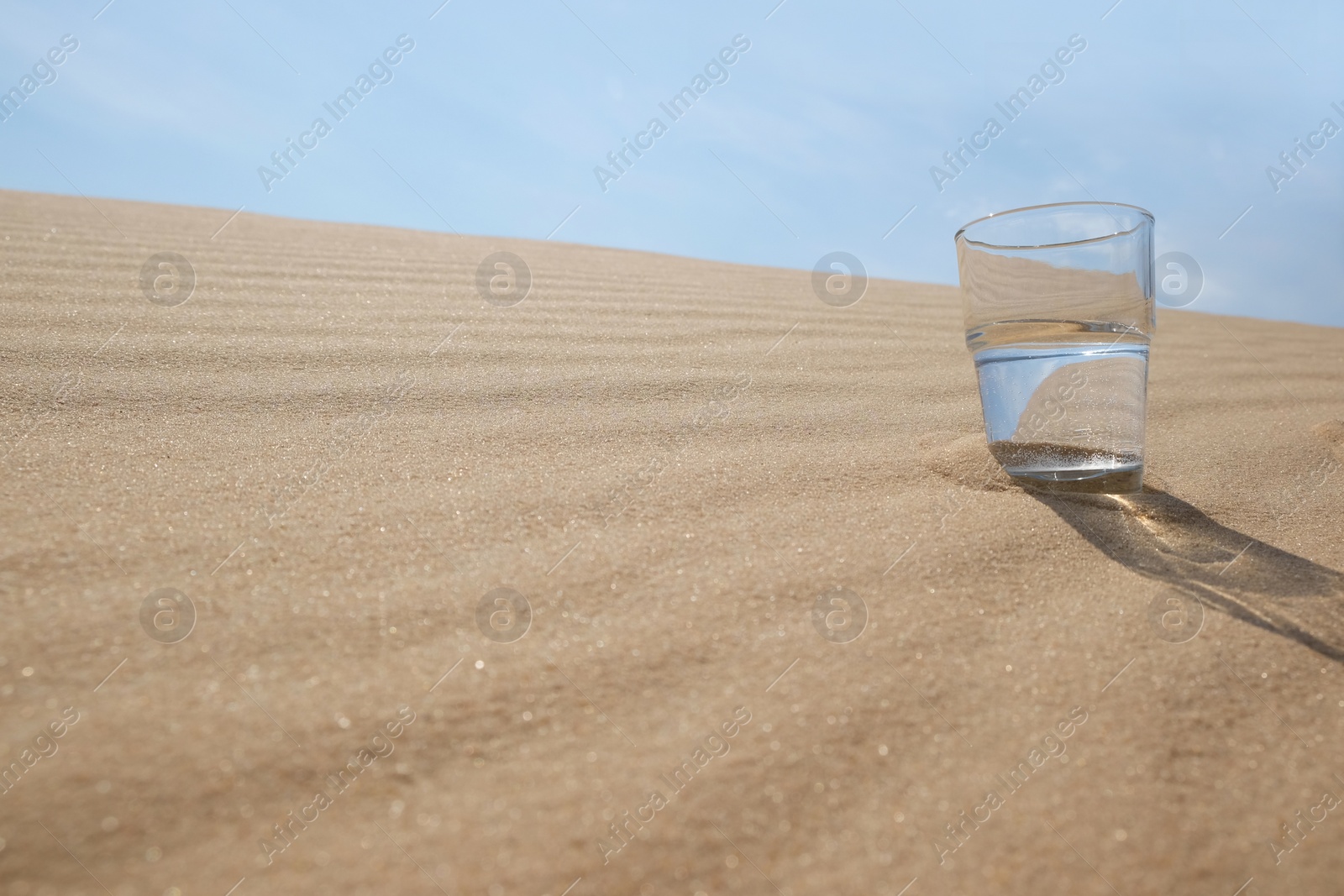 Photo of Glass of water on sand in desert. Space for text