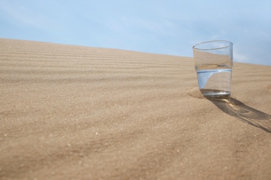 Photo of Glass of water on sand in desert. Space for text