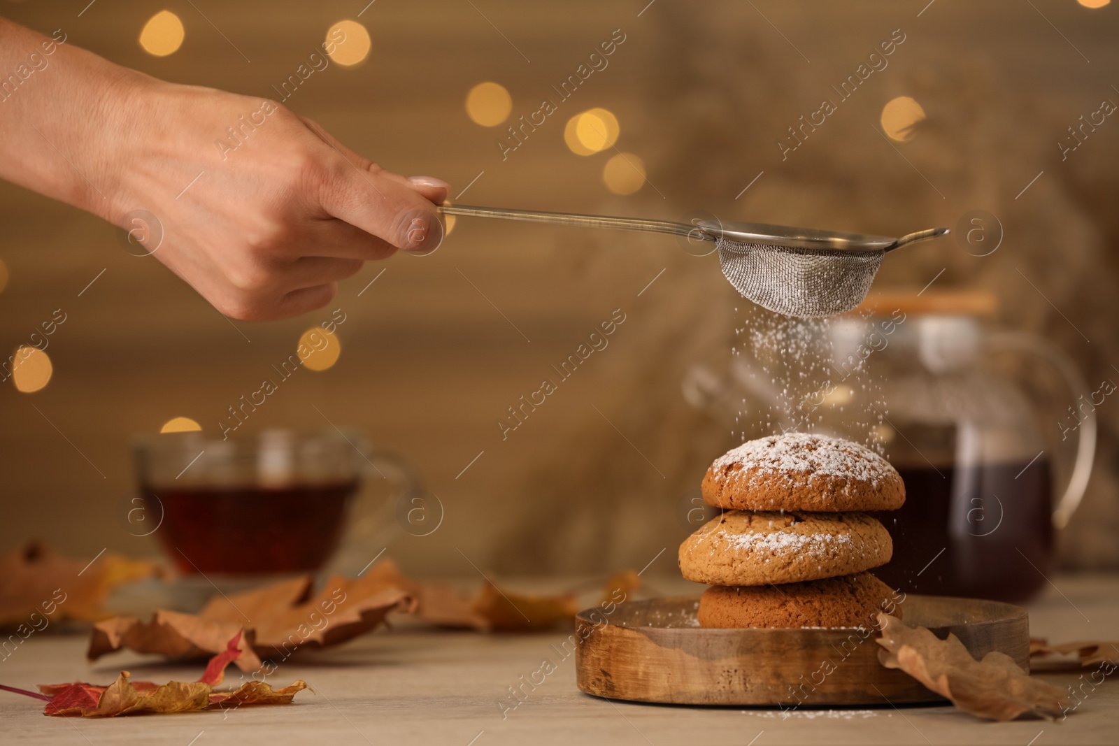 Photo of Woman sieving icing sugar on cookies at wooden table, closeup