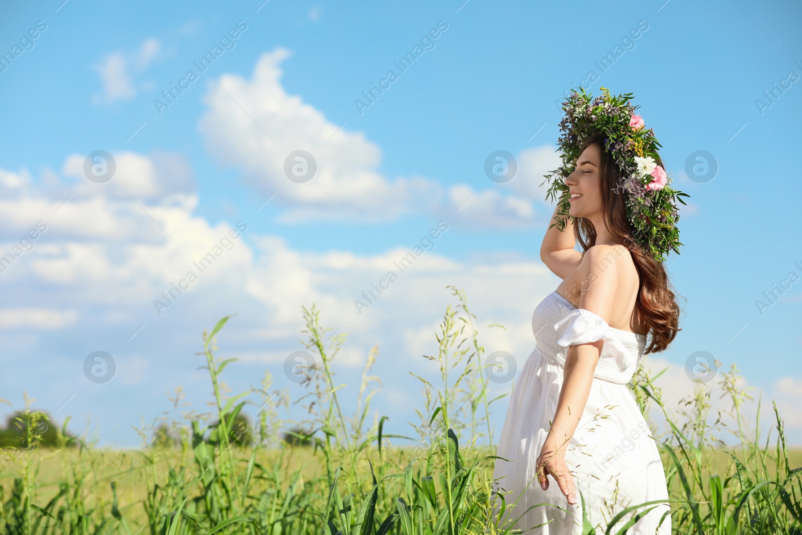 Photo of Young woman wearing wreath made of beautiful flowers in field on sunny day