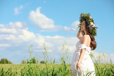 Young woman wearing wreath made of beautiful flowers in field on sunny day