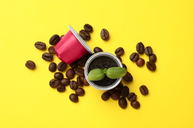 Coffee capsules with seedling and beans on yellow background, flat lay