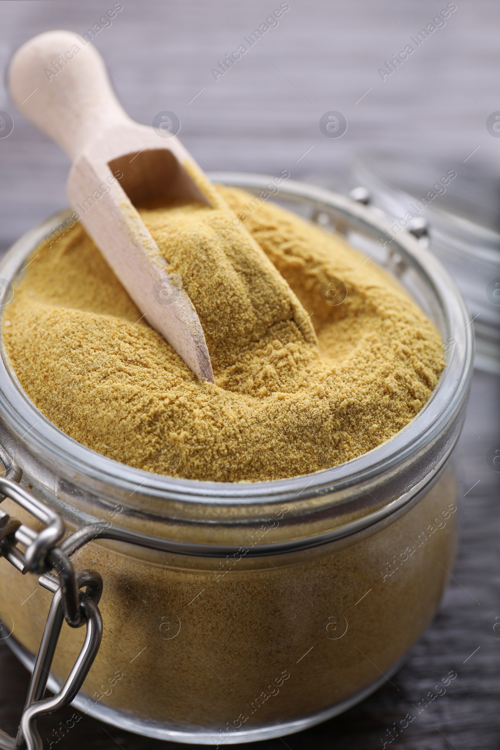 Photo of Scoop and glass jar with granulated brewer`s yeast on wooden table, closeup