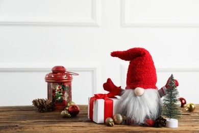 Photo of Cute Christmas gnome, gift box and festive decor on wooden table. Space for text