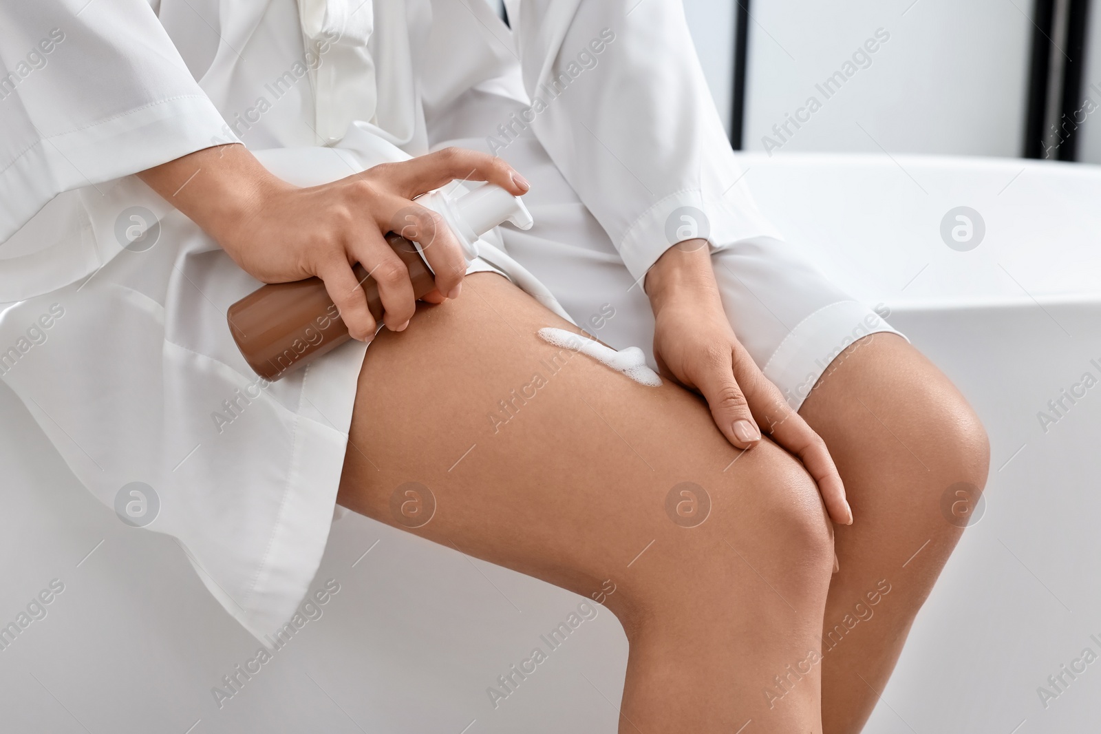 Photo of Woman applying self-tanning product onto her leg on tub in bathroom, closeup