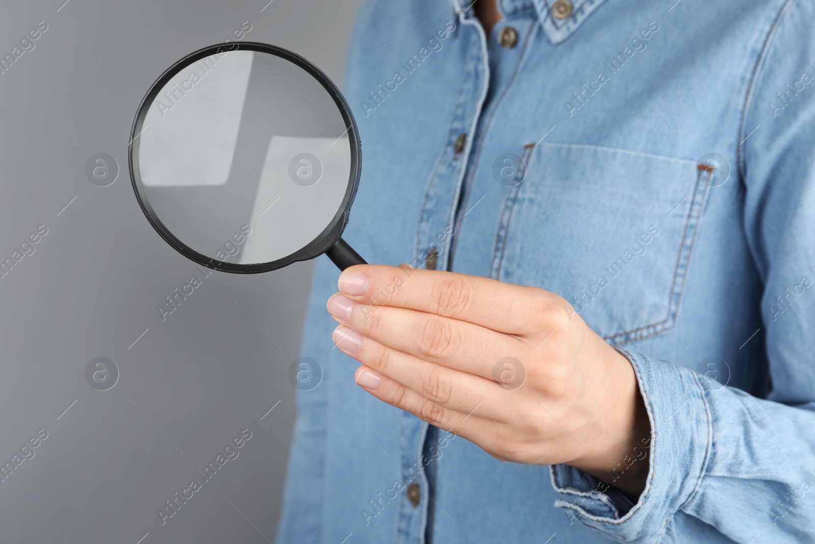 Photo of Woman holding magnifying glass on grey background, closeup. Find keywords concept