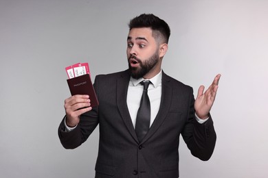 Surprised businessman with passport and tickets on grey background