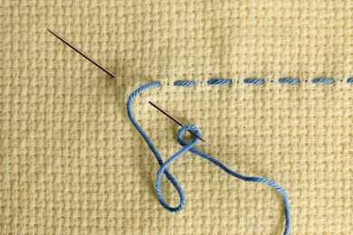 Photo of Canvas with embroidery thread and needle, top view