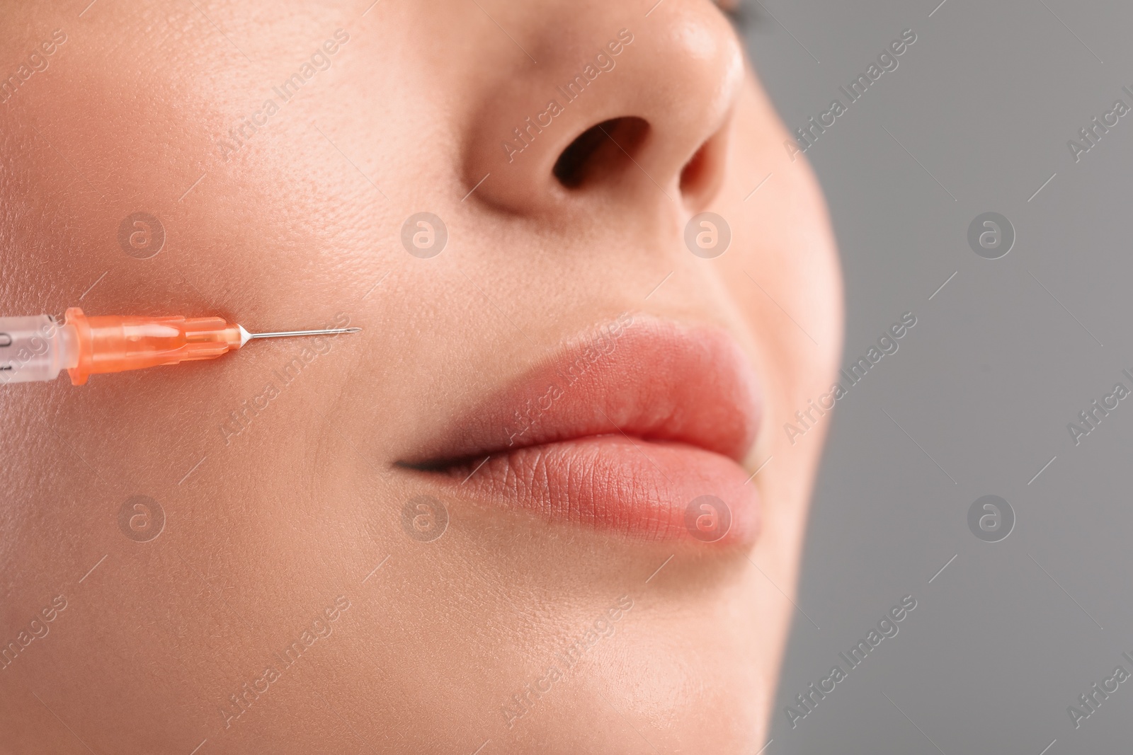 Photo of Young woman getting facial injection on light grey background, closeup. Cosmetic surgery