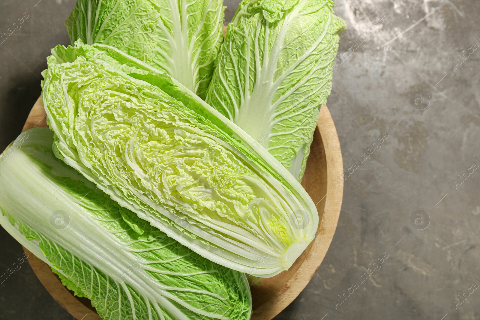 Photo of Fresh ripe Chinese cabbages in bowl on gray textured table, top view. Space for text