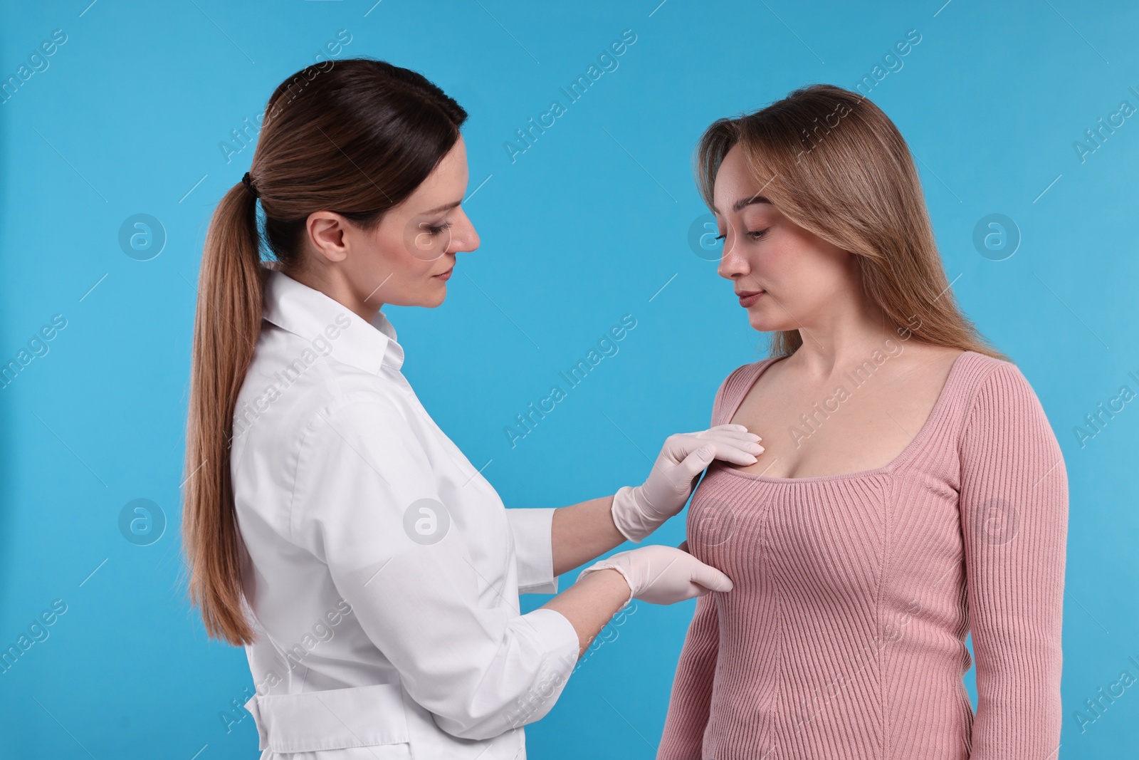 Photo of Mammologist checking woman's breast on light blue background