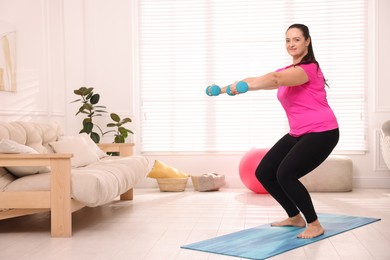 Photo of Overweight woman doing exercise with dumbbells at home, space for text