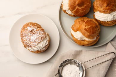 Delicious profiteroles with cream filling and powdered sugar on white marble table, flat lay