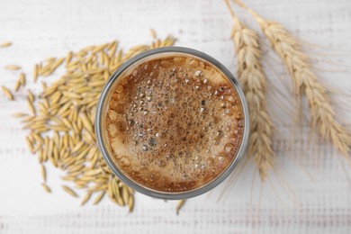 Cup of barley coffee, grains and spikes on white table, flat lay