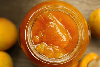 Photo of Jar of delicious jam and apricots on wooden table, closeup. Fruit preserve