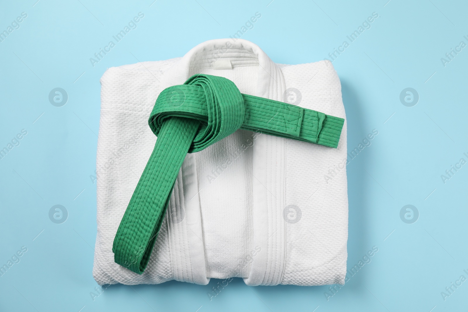 Photo of Green karate belt and white kimono on light blue background, top view