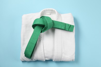 Photo of Green karate belt and white kimono on light blue background, top view