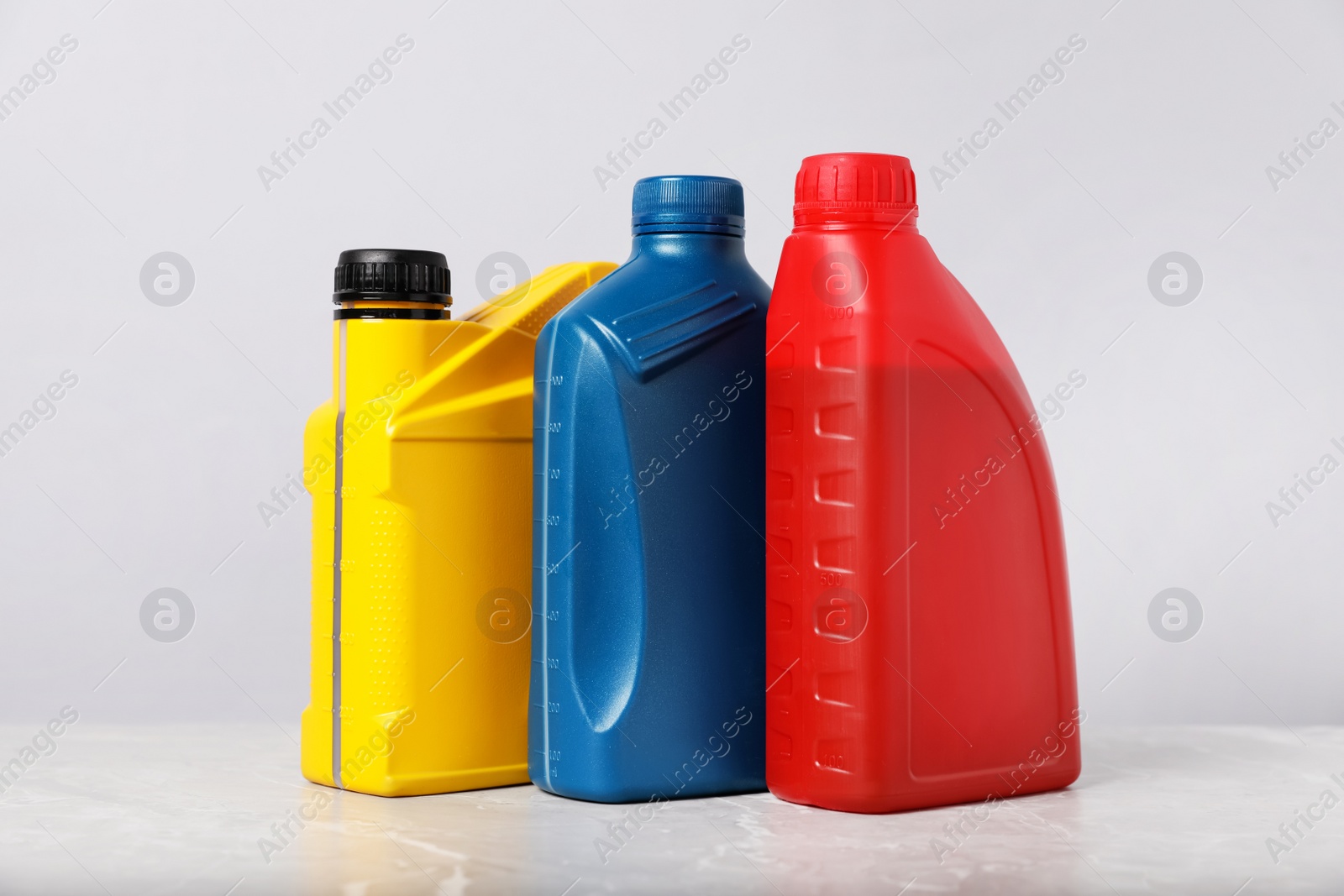 Photo of Motor oil in different canisters on grey marble table against light background