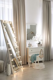 Photo of Large mirror with light bulbs and chest of drawers in stylish room. Interior design