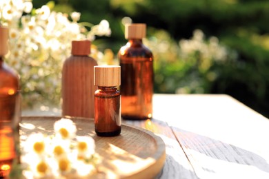 Bottles of essential oil and flowers on white wooden table outdoors, space for text