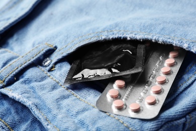 Photo of Black condom and birth control pills in pocket of jeans, closeup. Safe sex concept