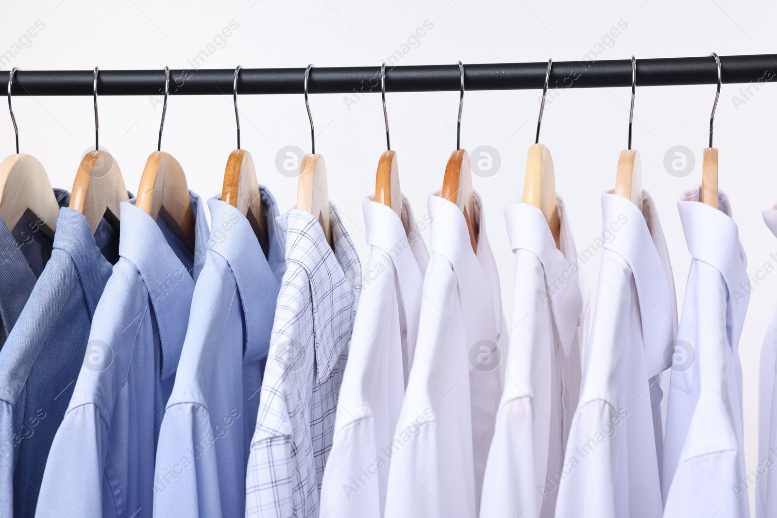 Photo of Dry-cleaning service. Many different clothes hanging on rack against white background, closeup