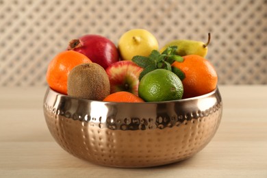 Photo of Fresh ripe fruits in metal bowl on wooden table, closeup