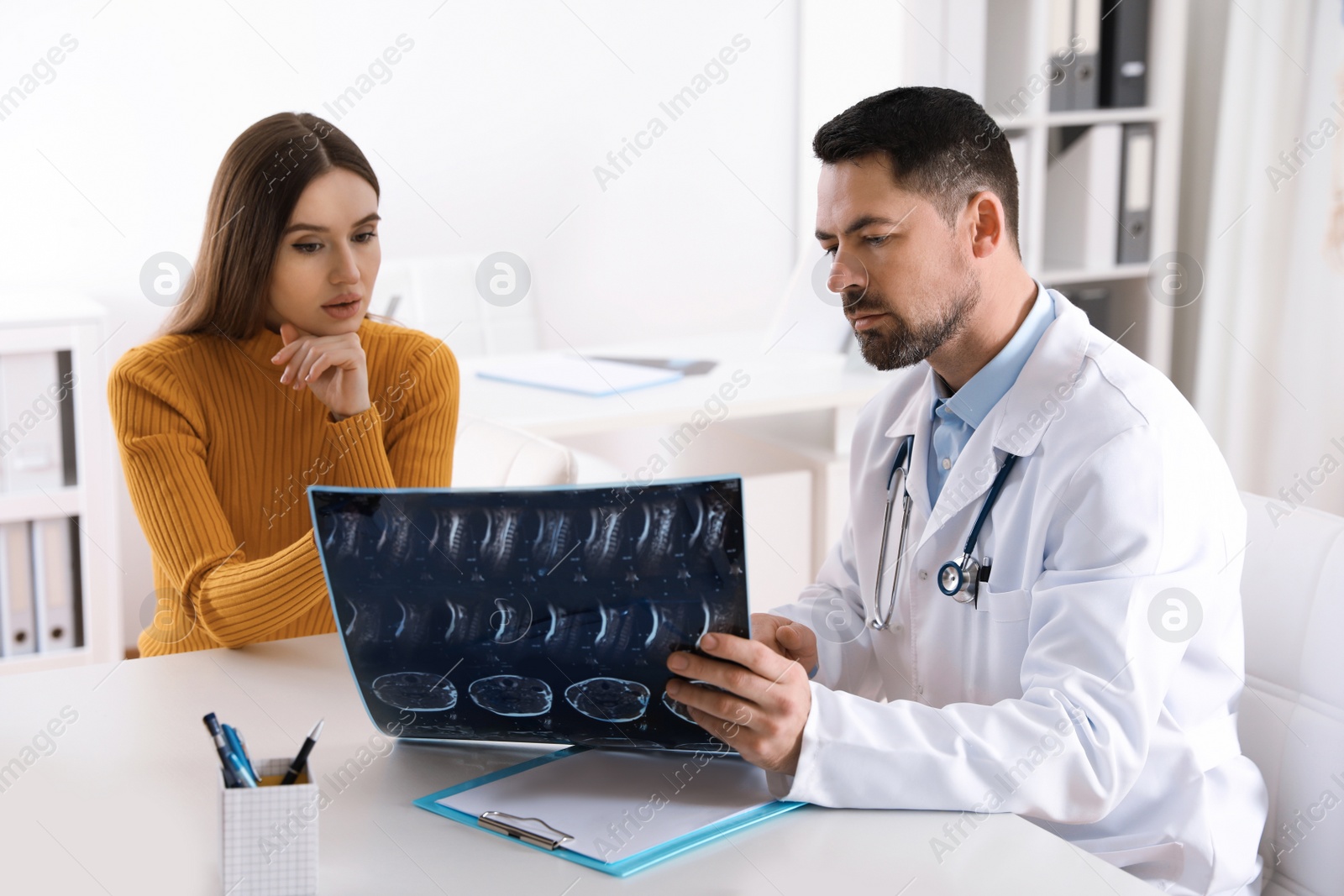 Photo of Orthopedist showing X-ray picture to patient at table in clinic