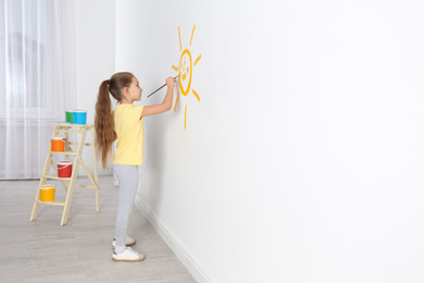Photo of Little child painting sun on white wall indoors, space for text