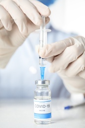 Doctor filling syringe with vaccine against Covid-19 at table, closeup