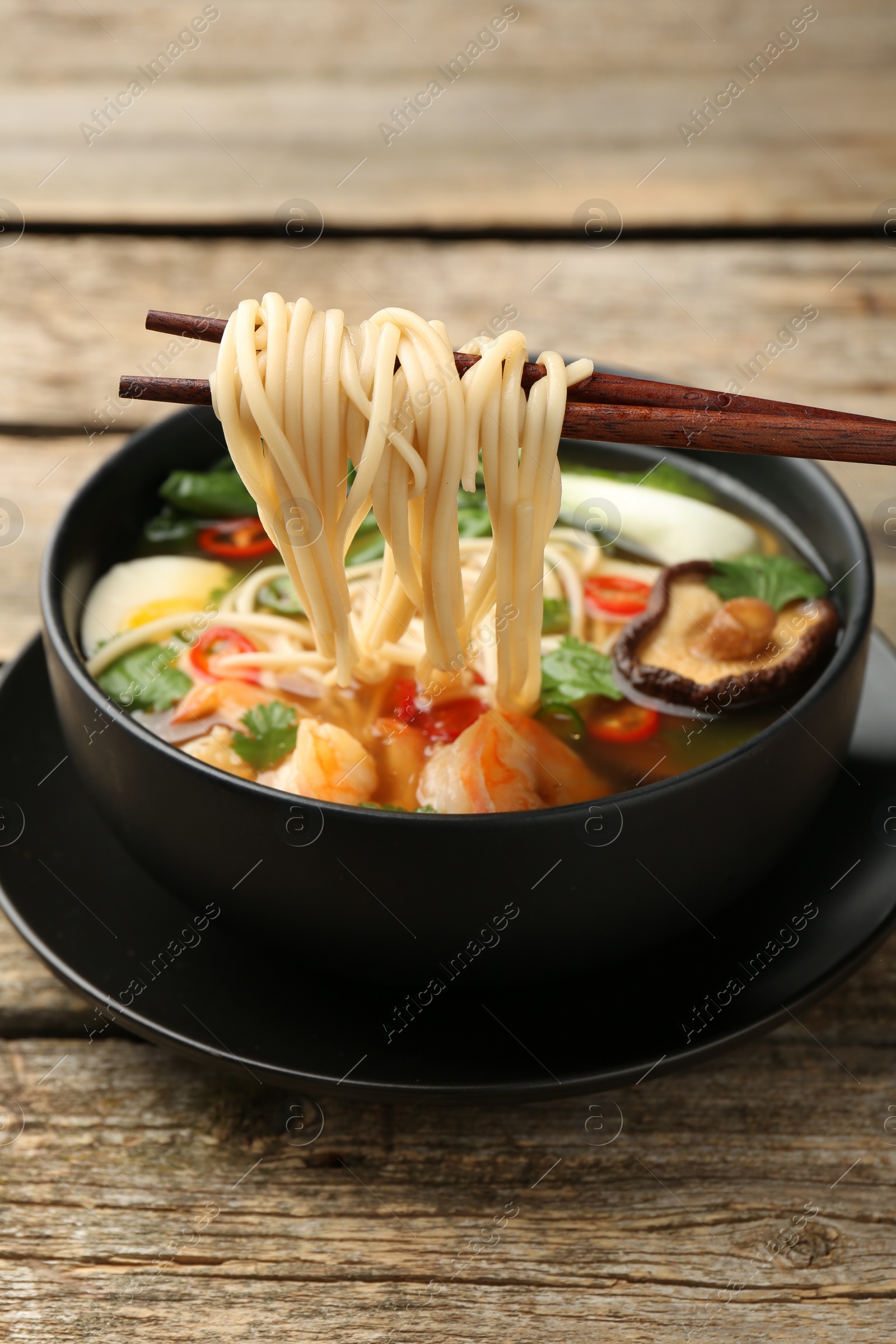 Photo of Eating delicious ramen from bowl with chopsticks at wooden table. Noodle soup